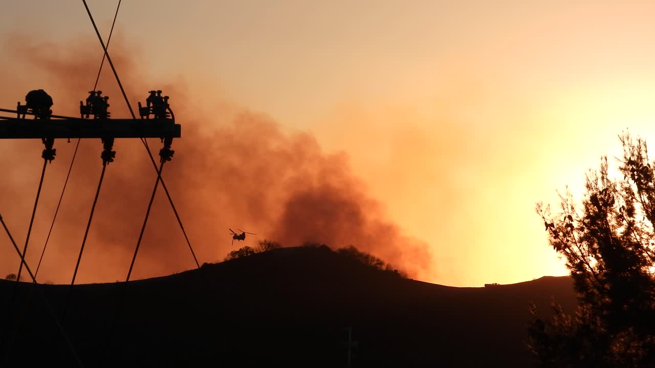 Apocalyptic silhouette of smoke rising off mountains at sunset, army helicopter silhouette flying above