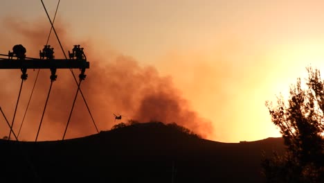 apocalyptic silhouette of smoke rising off mountains at sunset, army helicopter silhouette flying above