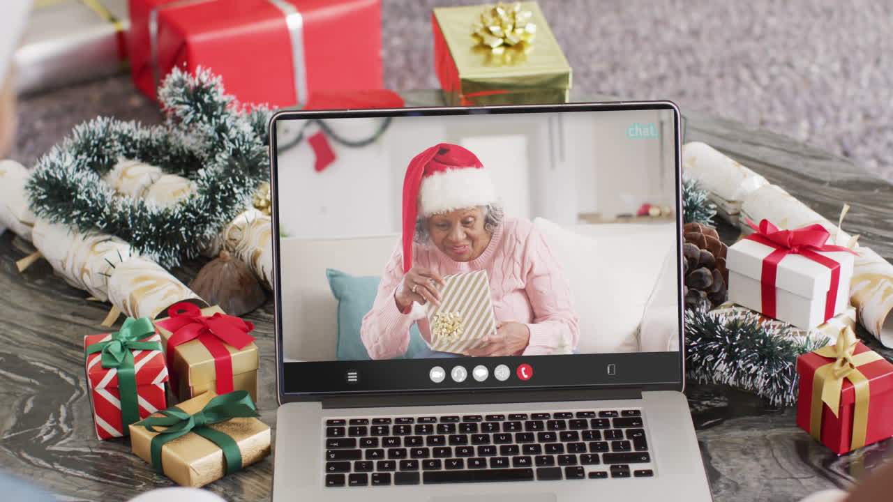 animación de mujer biracial en sombrero de santa en llamada de video portátil con amigos en navidad