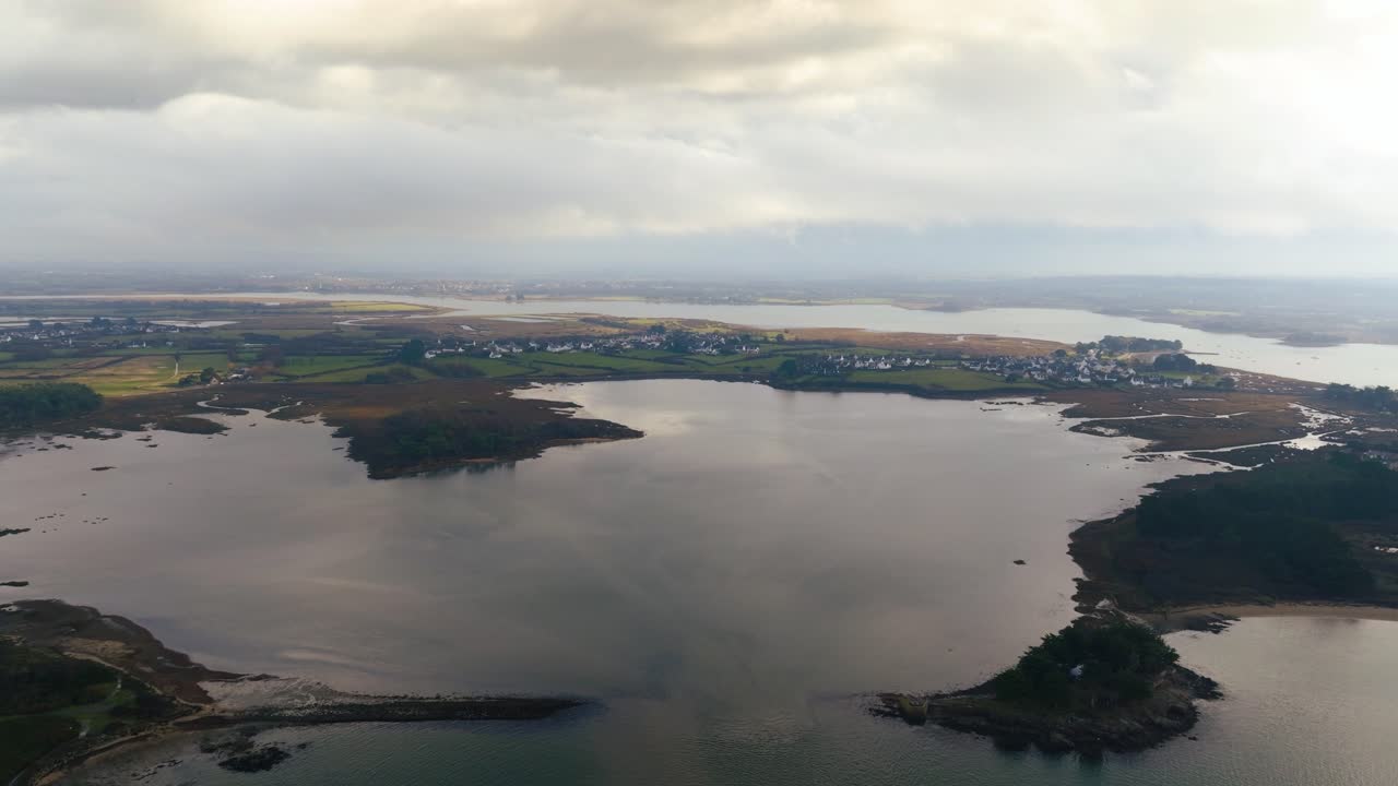 Panorama aereo della costa del Golfo di Morbihan in Bretagna, Francia, con acque calme che riflettono un cielo nuvoloso e isole sparse. Pittoresco ambiente costiero francese.