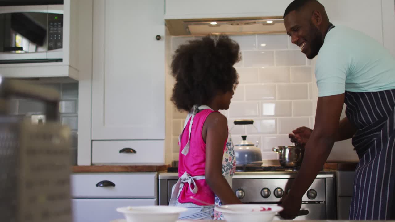 hija afroamericana y su padre cocinando juntos y dando cinco en la cocina