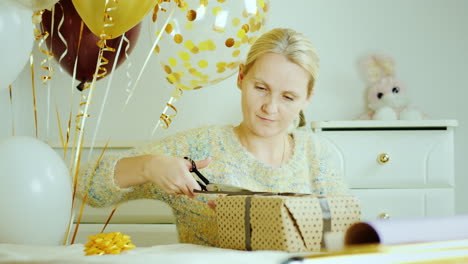 mamá envuelve una caja con un regalo en papel de envolver sentada junto a la cama en la habitación de los niños decorada con