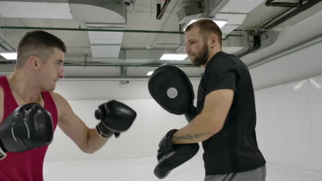 Cámara-Lenta:-Golpe-De-Potencia-A-La-Pata-De-Boxeo.-Fuerte-Atleta-Tatuado-En-Ropa-Deportiva-Entrenando-En-Patas-De-Boxeo-Con-Pareja