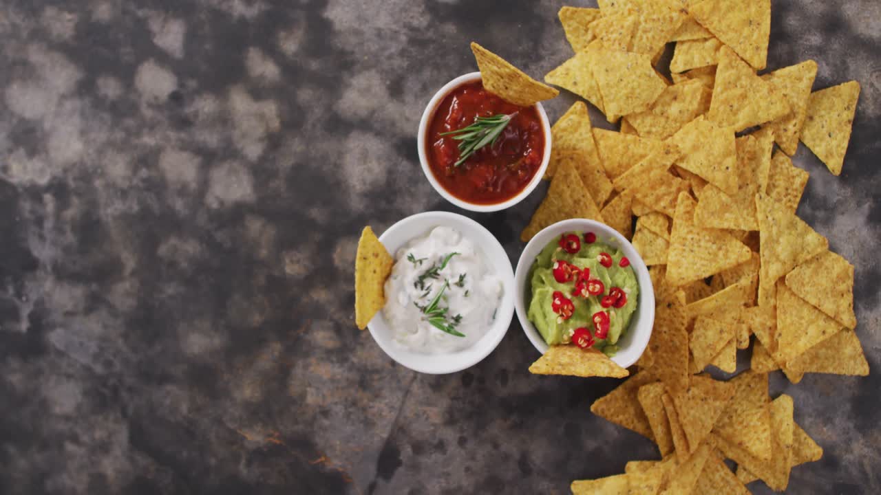 Plano detalhe de nachos e variedade de molhos em superfície preta