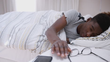 man asleep in bed reaches out to turn off alarm on mobile phone