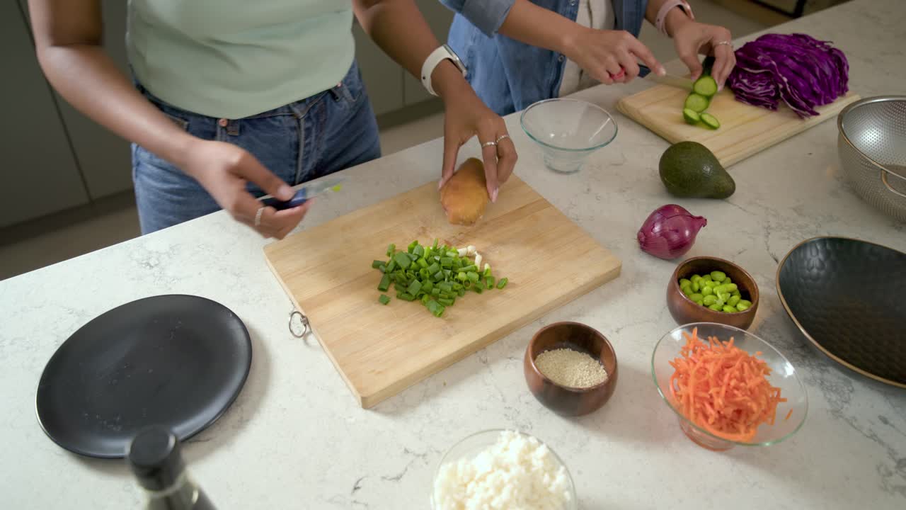 Amiche che preparano il cibo, tagliano le verdure e affettano patate dolci sull'isola della cucina