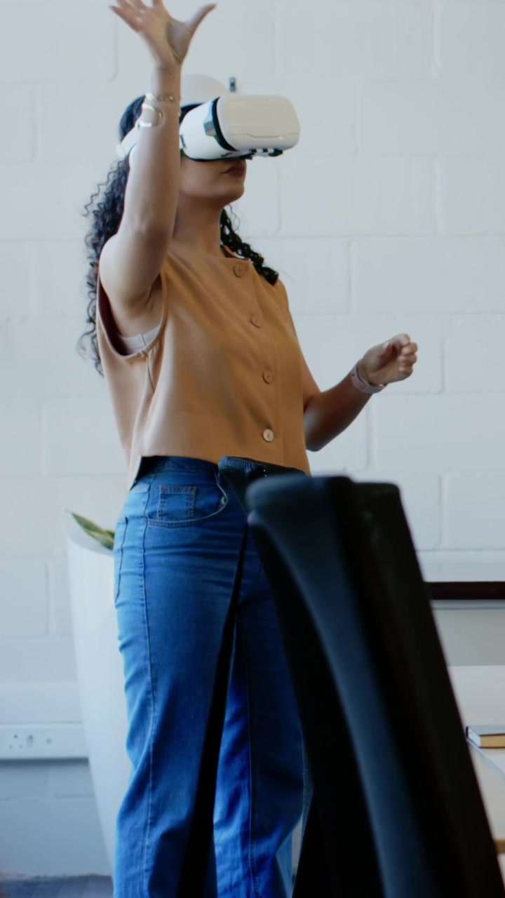 Video verticale: Una donna mette un visore VR bianco e gesticola per manipolare oggetti virtuali in ufficio.