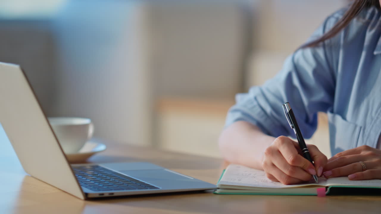Woman hand writing notes working at home kitchen closeup. Lady looking laptop