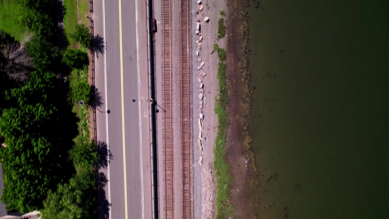 Un drone vola guardando dritto in basso dall'alto una strada, dei binari del treno e una costa fluviale a Salem, Massachusetts