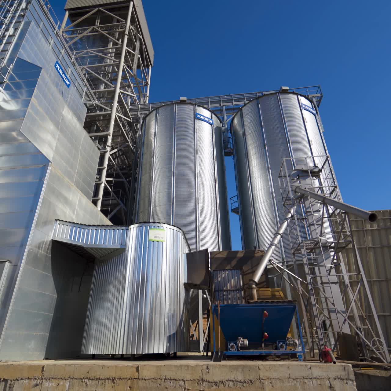 Metal grain elevator in agricultural zone. Silver silos on agro manufacturing plant for processing drying cleaning and storage of agricultural products