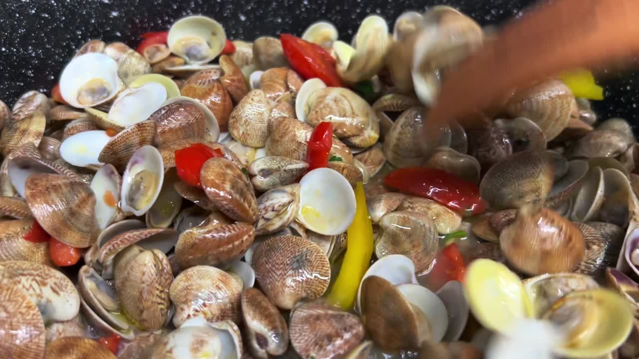 mezclando deliciosas almejas frescas pimientos y tomates con tenedores de madera en sartén caliente