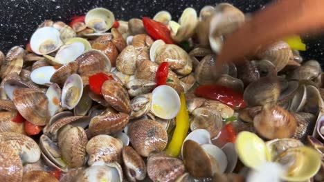 mezclando deliciosas almejas frescas pimientos y tomates con tenedores de madera en sartén caliente