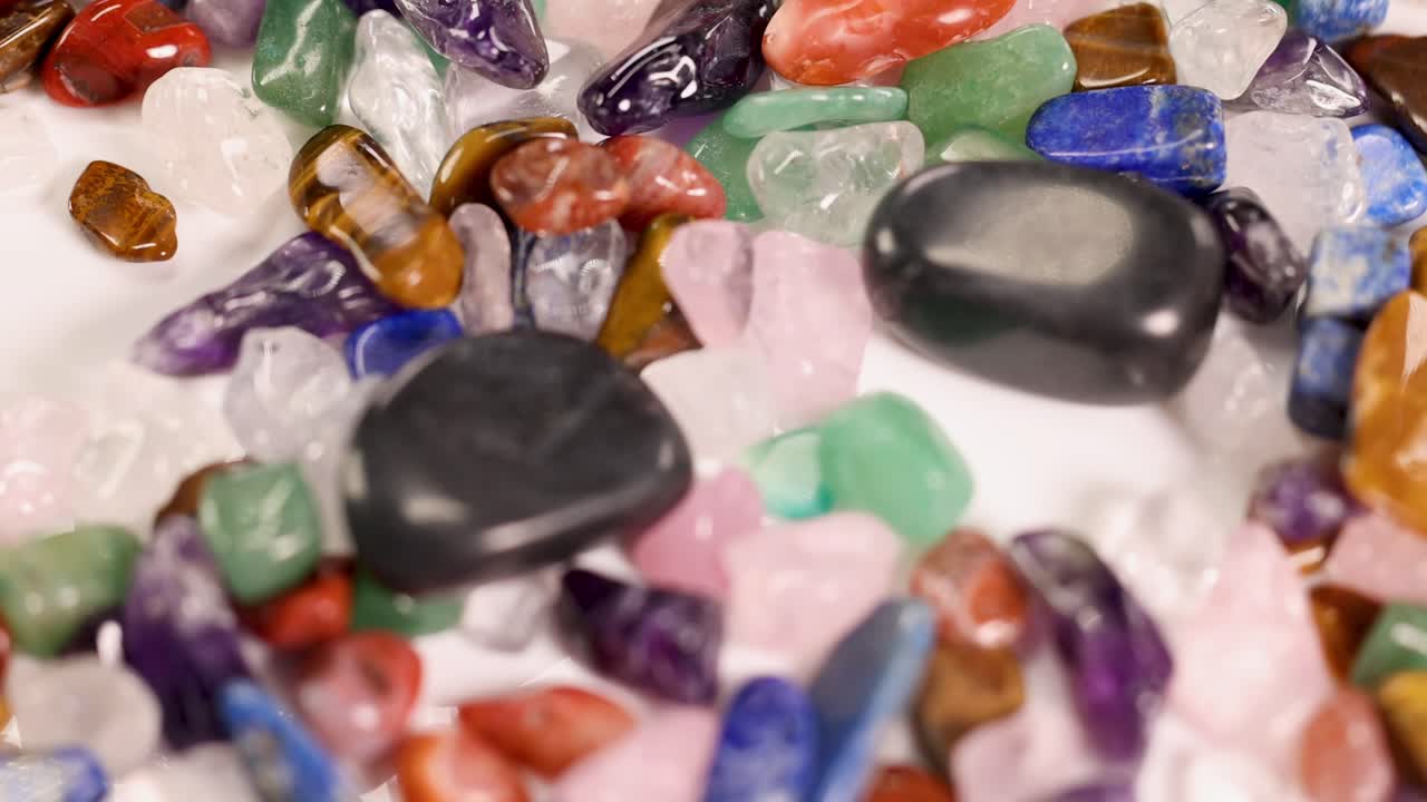 A collection of vibrant gemstones is arranged and manipulated with tweezers, highlighting their colors and textures under bright lighting