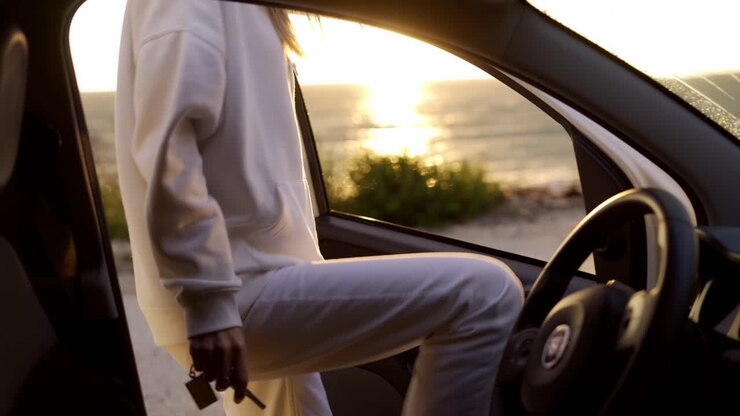 Femme blonde montant en voiture sur la côte à l'heure dorée