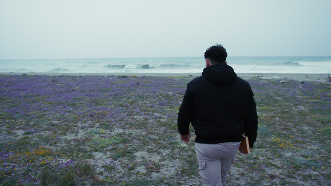 Man Walks Toward The Winter Sea With A Book In Hand