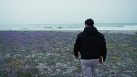 man walks toward the winter sea with a book in hand