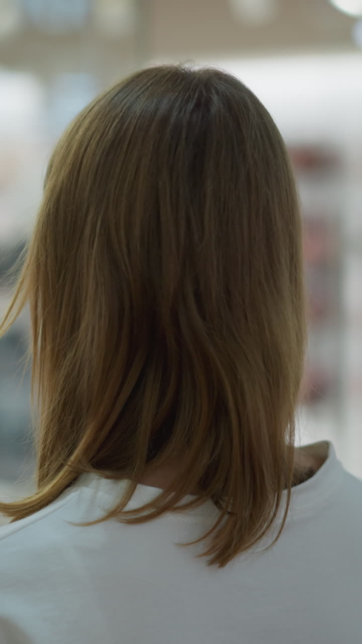 쇼핑몰의 옷 가게 앞에 서 있는 여인이 바지와 브래지어를 입은 마네킨을 관찰하고 있으며, 잘 조명된 소매 환경에서 옷의 랙을 특징으로하는 흐릿한 배경이 있습니다.