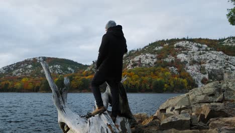 Young-Man-Explores-Stunning-Autumn-Nature-Wilderness-on-a-Blue-Lake-in-Canada,-Wide-Handheld-Pan-at-Cloudy-Sunset