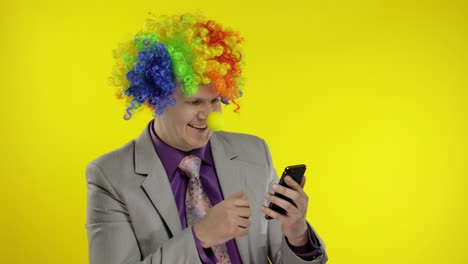 payaso empresario empresario con peluca usando una aplicación en el teléfono inteligente para el trabajo en línea