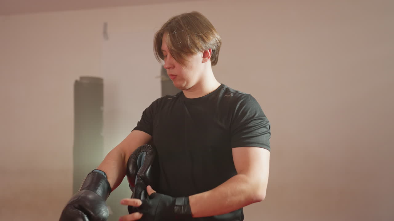 MMA fighter prepares for training session by putting on black boxing gloves over protective hand wraps, focusing on readiness, discipline, and strength inside gym environment with determination