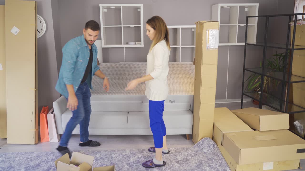 Smiling young couple move into a new home sitting on floor and unpacking.