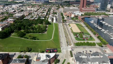 Aerial-dolly-shot-of-Federal-Hill-Historic-District,-American-flag-in-summer-breeze,-Baltimore-Maryland-Inner-Harbor-marina-and-boats,-docked,-residences-and-homes-in-urban-city-in-United-States