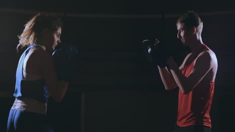 Hermosa-Boxeadora-Morena-Entrenando-Golpes-En-Las-Patas-Con-Un-Entrenador-En-Un-Cuarto-Oscuro