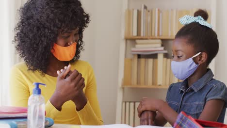 African-american-mother-and-daughter-wearing-face-mask-sanitizing-their-hands-at-home