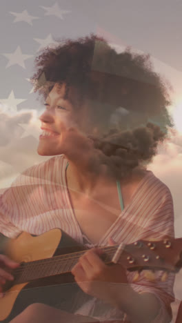 animation of flag of united states of america over happy biracial woman playing guitar on beach