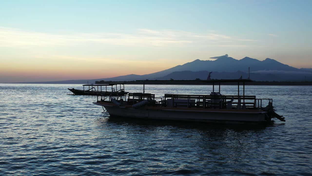 발리에서 밝은 하늘이 반사되는 일몰 후 열대 섬 해안 근처의 잔잔한 바닷물에 떠 있는 정박된 배들
