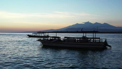 barcos anclados flotando en aguas tranquilas cerca de la costa de la isla tropical después de la puesta del sol con un cielo brillante que se refleja en bali