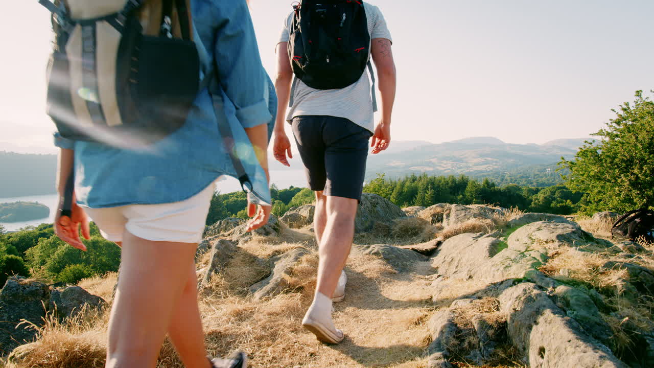 cámara lenta vista trasera de la pareja joven de pie en la cima de la colina mirando el hermoso campo en una caminata a través del distrito de los lagos en el reino unido