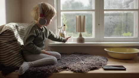 a child sits listening and perhaps watching and drinking water by a sunny window