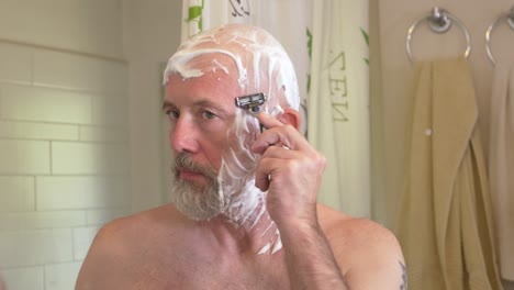 white male shaves his cheek with a razor in a bathroom