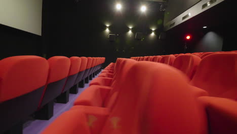 sideway view of red cinema armchairs in an empty movie theatre . smooth shot