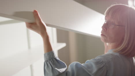 60 year old handywoman installs white shelving unit against wall, closeup