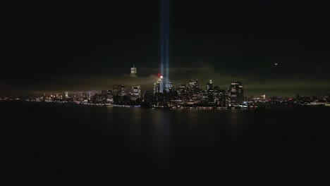 Eine-Luftaufnahme-Des-Freedom-Tower-Im-Finanzviertel-Von-New-York-City-Bei-Nacht,-Mit-Der-Hommage-In-Hellen-Doppelstrahlen-Beleuchtet