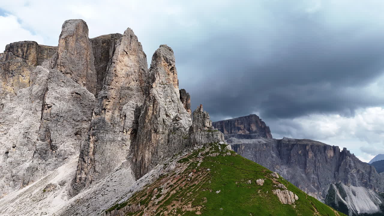 Vista aerea con drone di maestose torri di calcare che si ergono sopra prati alpini nelle Dolomiti, Italia, sotto un cielo di montagna nuvoloso.
