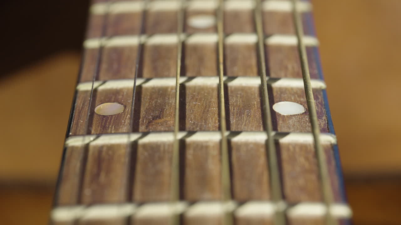 Primo piano estremo delle corde di una chitarra acustica e della tastiera in legno, con un'ombra drammatica che si muove sullo strumento. Ideale per documentari musicali e montaggi artistici.