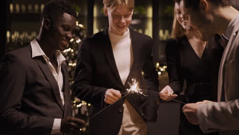 group of friends wearing stylish clothes and lighting sparklers at new year's eve party