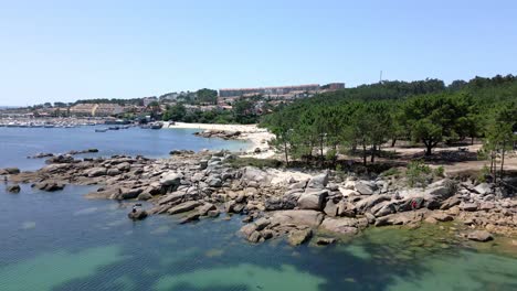 Toma-Aérea-De-Drones-De-Una-Tranquila-Playa-En-Un-Pueblo-Con-Puerto-Deportivo-Y-Bosque