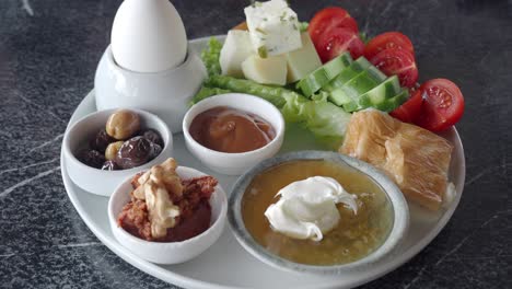 a turkish breakfast plate with eggs, cheese, olives, tomatoes, cucumber, honey, butter, jam, walnuts, pastry, and bread