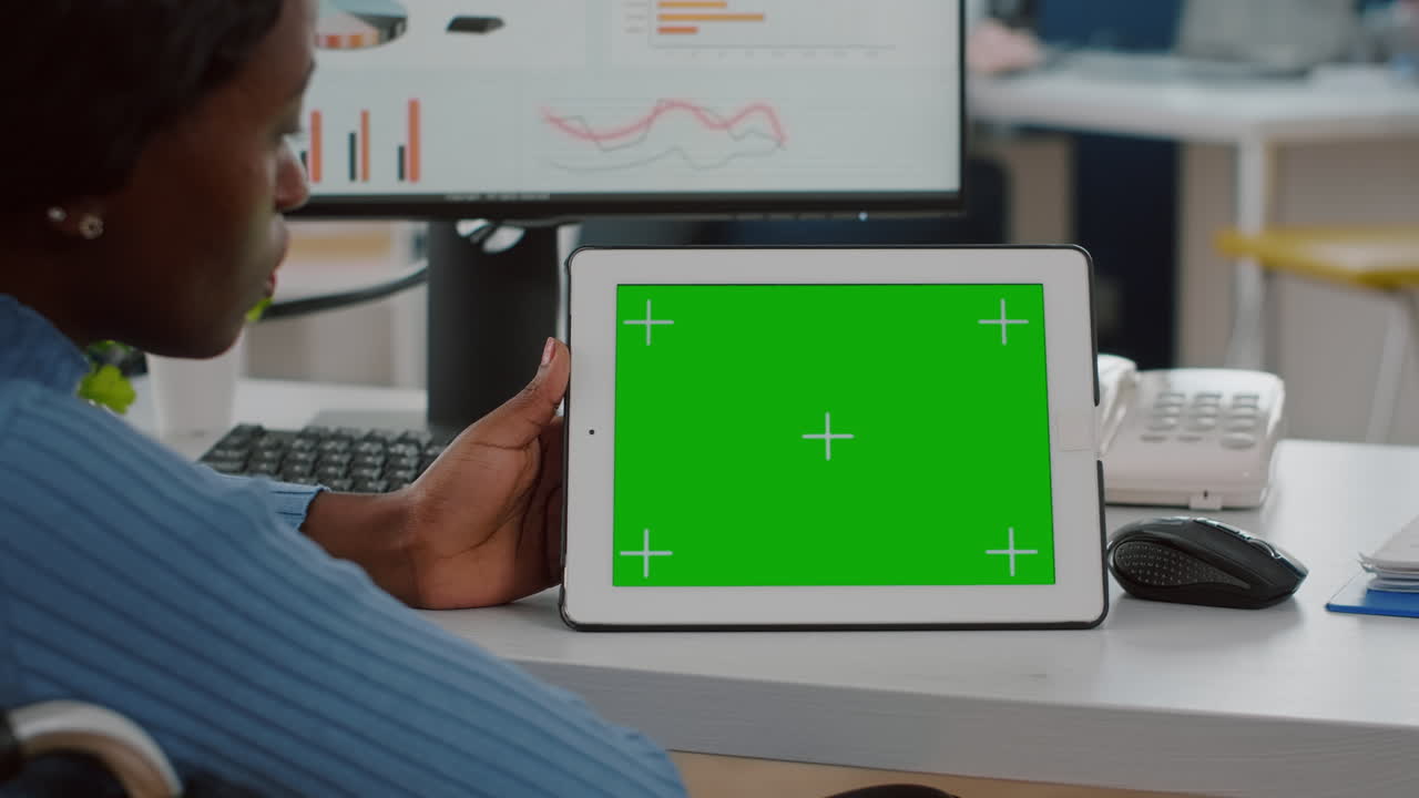 Handicapped african employee in wheelchair looking at tablet with green screen