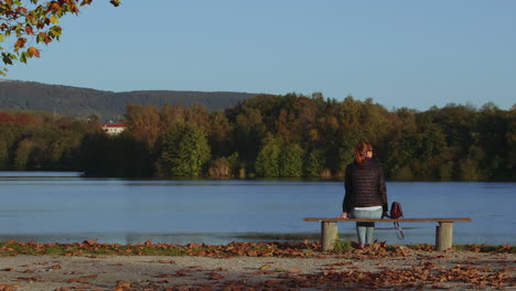 attractive girl walks to bench and sits to have a view on lake, static