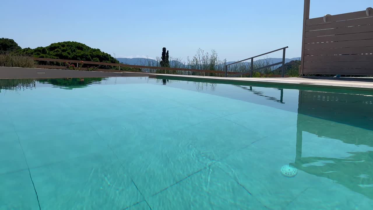 En klar, blå swimmingpool på et boutiquehotel i bjergene i Zakynthos, Grækenland. Kameraet hæves langsomt for at afsløre en bugt i Middelhavet, der fremkalder luksus, afslapning og flugt.