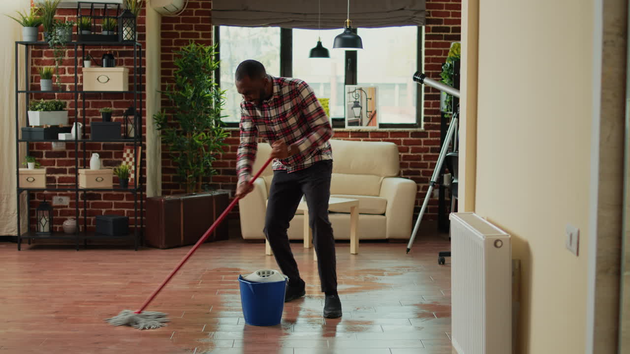 Cheerful boyfriend dancing and washing floors with all purpose cleaner