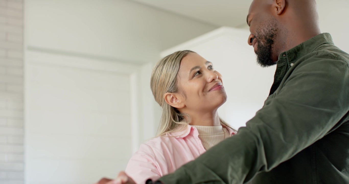 African American couple in pink green shirts holding hands man leaning sharing soft gaze in kitchen