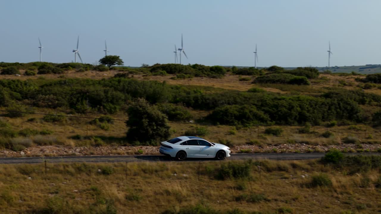 Auto bianca su strada di campagna con turbine eoliche