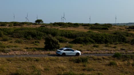 white car on country road with wind turbines