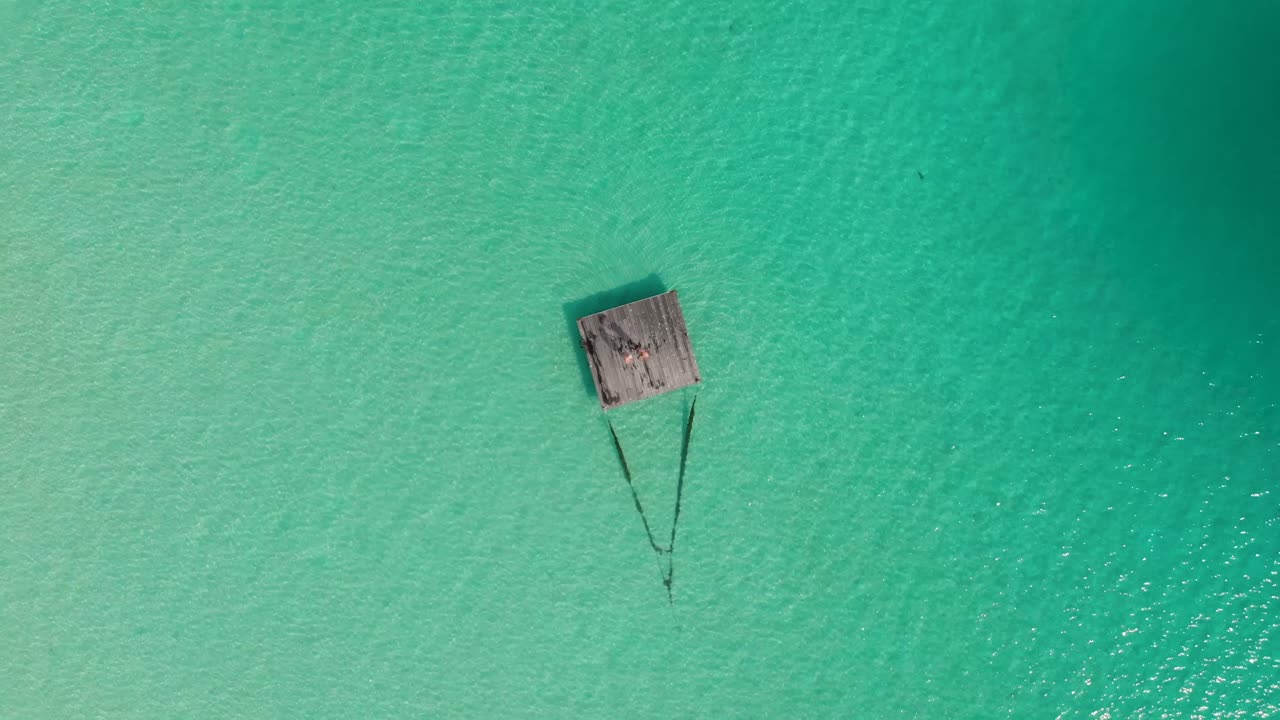 Piccolo pontile di legno remoto nel mezzo di una laguna esotica con una coppia in piedi, ripreso dall'alto